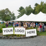 A large white tent on a lawn with blank white signs: "your logo here"