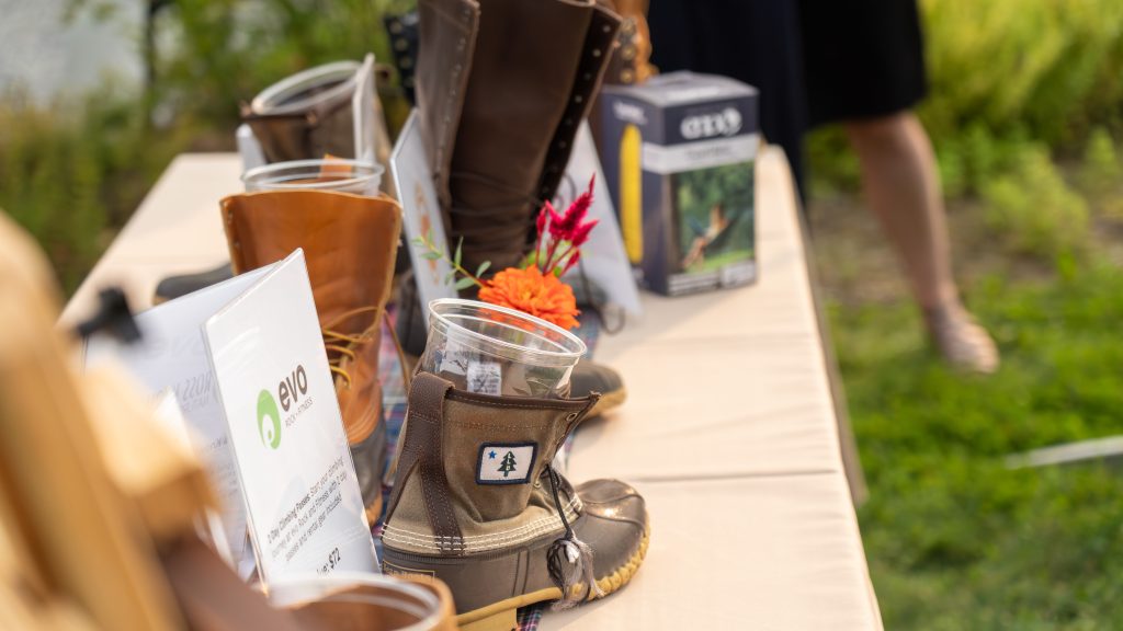 A display of various boots, decorated with flowers and signage for Evo Rock Fitness, set outdoors on a table.