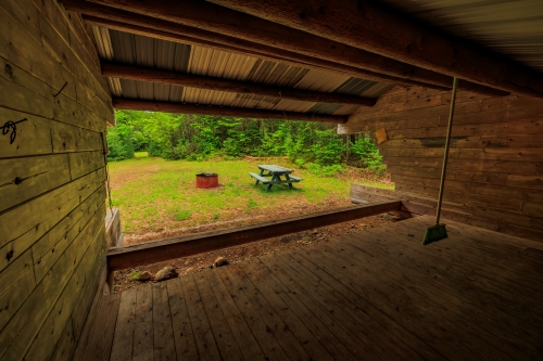 Looking out from the inside of a rustic wooden camping leanto towards a grassy field.