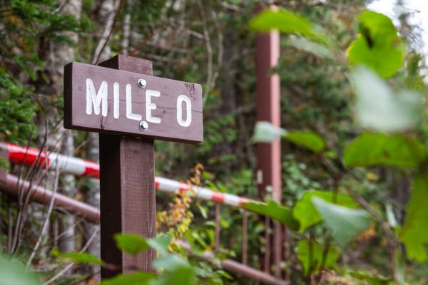 A wooden park sign says "Mile 0" in front of a road gate.