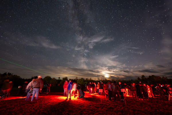Dozens of people are in a dark field lit by red lights under a dark sky.