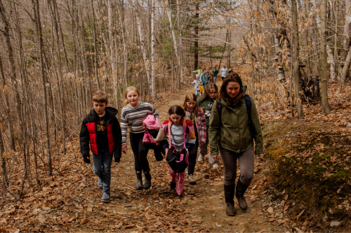 A group of children walk along a wooded path in spring.